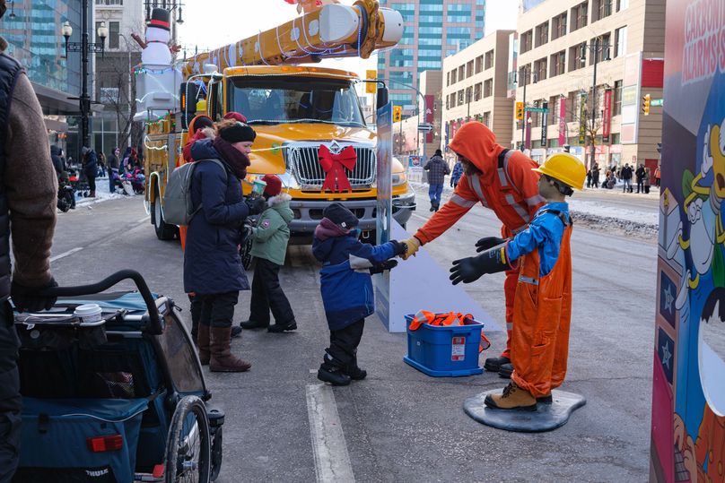 Un jeune enfant tend la main à un travailleur d’Hydro devant un camion-nacelle illuminé.