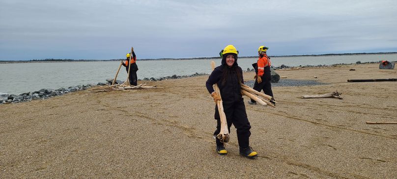 Three people haul driftwood from the shore line on an island’s sandy beach.