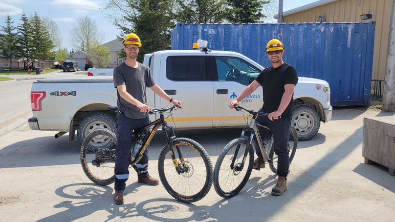 Deux hommes portant un casque de protection prennent la pose sur des vélos de montagne devant un camion de Manitoba Hydro.