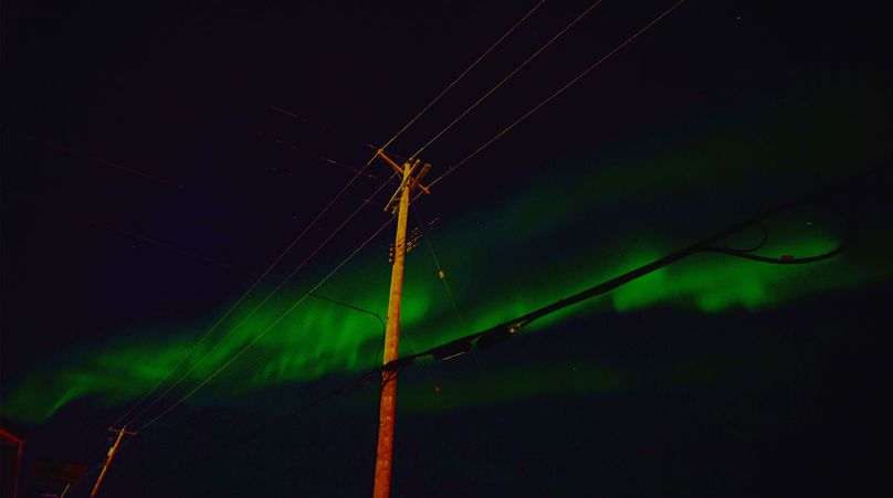 Northern Lights or Aurora Borealis dancing in the night sky, showcasing vibrant colours of green, with a backdrop of hydro pole.